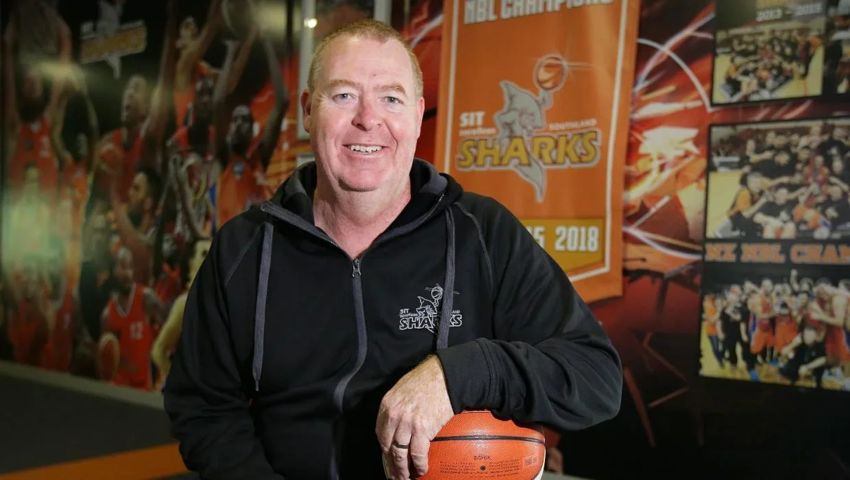 Rob Beveridge portrait with basketball and championship banners
